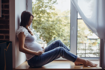 pregnant brunette girl sitting on the windowsill