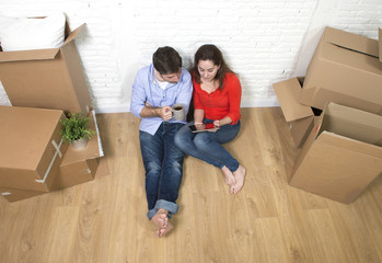 Fototapeta na wymiar young couple sitting on floor moving in new house using digital