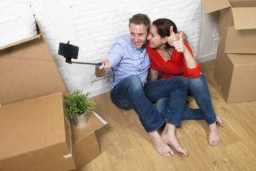 Fototapeta na wymiar young happy American couple sitting on floor celebrating moving to new house taking selfie photo with mobile phone