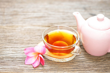 Tea in glass and pink teapot with flower on wooden table