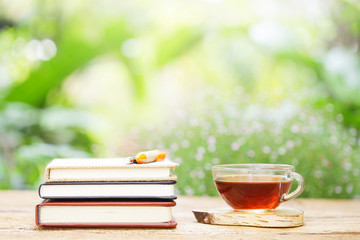 tea in glass and notebook with pens on wooden table at outside