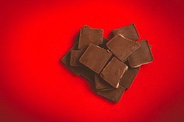 Pieces of chocolate in heart shape on red background