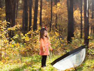 Little girl in the autumn forest with a transparent umbrella