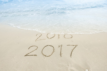 New Year 2017 coming, 2016 and 2017 on a beach sand, the wave is