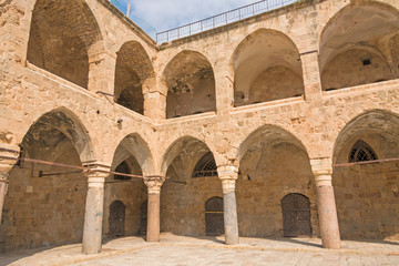 Fototapeta na wymiar Arched gallery of Khan al-Umdan viewed from paved courtyard. Old city of Acre, Israel. 