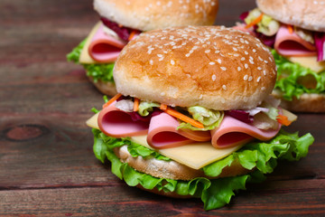 Burger sandwich with sausage, cheese and vegetables on a wooden background