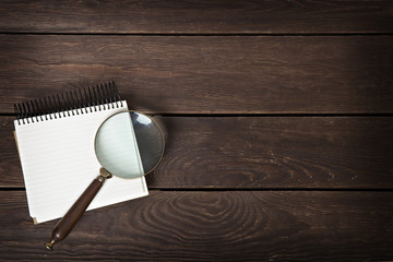 notebook with a magnifying glass on a wooden background - obrazy, fototapety, plakaty