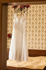 Beautiful  wedding dress hanging on a lamp in the room. Bridal morning.