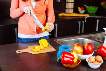Young woman chopping pepper in kitchen