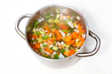 chopped soup ingredients: carrots, onions and celery cooking in a stainless steel pot