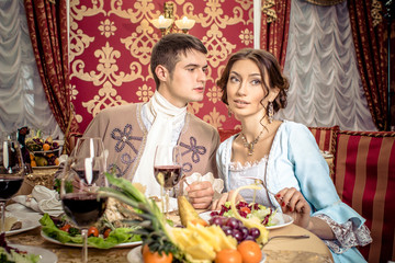 young man in a historic jacket and girl in vintage dress sitting at the richly laid table in a restaurant. Elegant vintage couple in restaurant. Retro couple portrait. Romantic Beauty.Vintage Styled