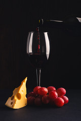 Glass with wine, a pice of cheese and bunch of grapes