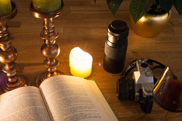 Open book, burning candles, a photo camera and a glass of red wine on a table on dark