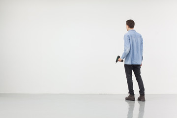 Man holding a drilling machine standing in front of a white wall