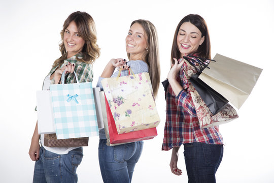 Three attractive young women with shopping bags on white background,smiling on camera.