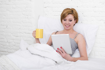 attractive woman on bed using digital tablet pad reading morning online news in internet having coffee