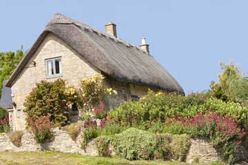 Fototapeta na wymiar Traditional thatched roof stone Cotswold cottage with roses on the wall and flowers in the garden