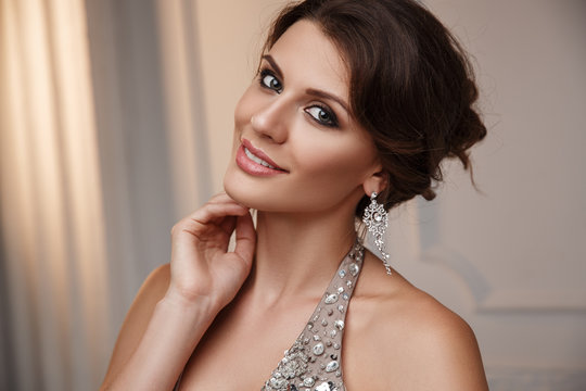 Portrait of a smiling smart dressed young beautiful woman in the elegant evening dress and expensive earrings jewelry with expressive make up