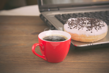 donut, coffee and a laptop on an old wooden table, toned