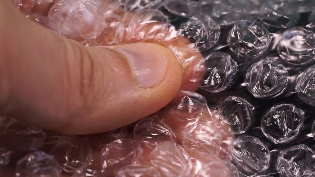 Fingers bursting air pockets in a sheet of transparent bubble wrap. clip recorded with macro lens and shallow depth of field