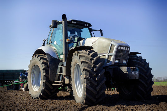 closeup side view tractor on big wheels on ploughed field