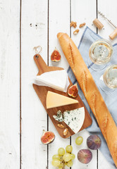Verschiedene Käsesorten (Brie, Parmesan, Blauschimmelkäse) Baguette, zwei Gläser Weißwein, Feigen und Trauben. Weißer Holztisch als Hintergrund. Romantische französische Picknicklandschaft von oben eingefangen.