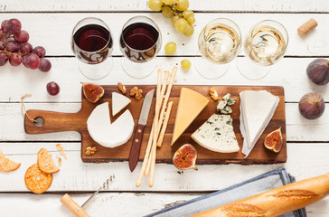 Red and white wine plus different kinds of cheeses (cheeseboard) on rustic wooden table. French...