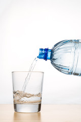 Vertical shot of hand pouring refreshing mineral water from bottle into glass