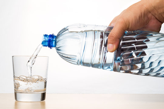 Hand pouring refreshing natural mineral water from bottle into glass