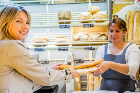 smiling woman with an apron selling bread to a client
