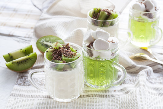 Vanilla panna cotta with kiwi and grated chocolate in glass, sliced kiwi on white wooden table