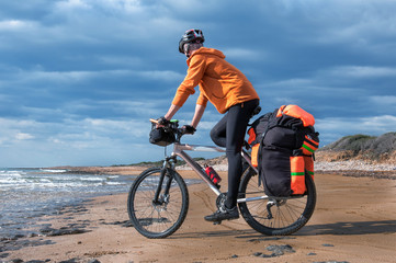 man goes  sandy beach on mountain bike with big backpack.