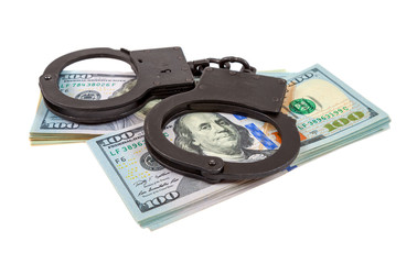 Steel handcuffs lying on a stack of dollar bills on the white ba
