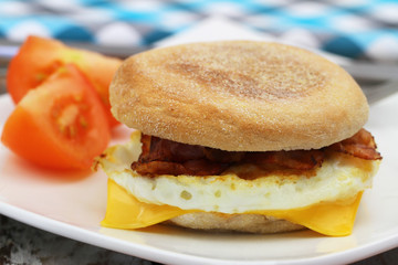 Egg and bacon muffin with tomato pieces on the side
