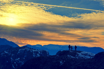 Group of people stands on the top of rock. Beautiful sunset clou