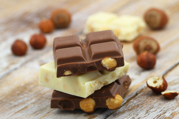 Milk and white chocolate with hazelnuts stacked up on rustic wooden surface
