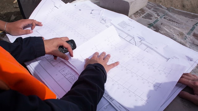 Building plan lying on the bricks. Engineers and construction workers studying drawing. Close-up