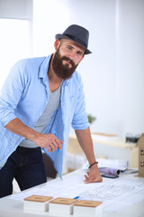 Portrait of male designer in hat with blueprints at desk 