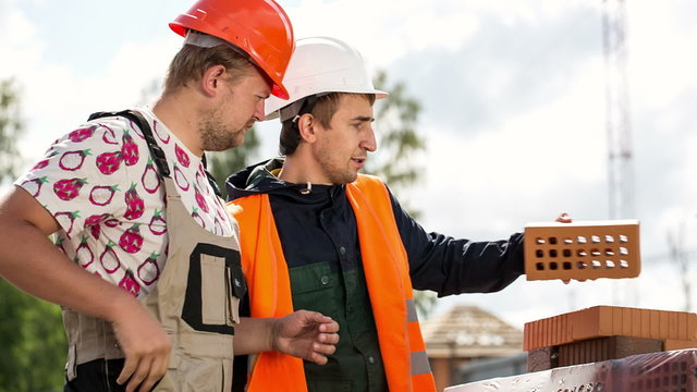 engineer and builder are on the construction site. Engineer demonstrates how to build.It takes a brick and features.It tells about the object. Perhaps teaching
