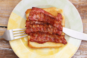 Crispy bacon on toast on plate, closeup
