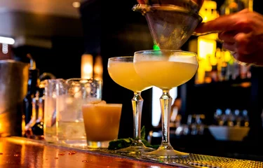 Rolgordijnen Cocktail wordt gegoten in een bar. Bewegingsonscherpte. Selectieve focus op het voorgrondglas. © Crin