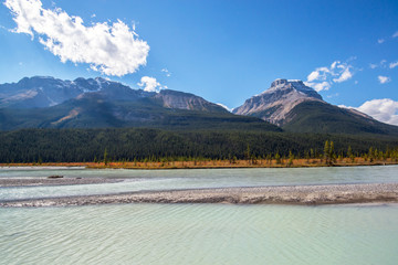 milky waters of a river in a valley in the middle of peaks and forest of pines during a sunny day in the rocky mountains of alberta canada