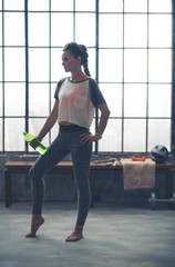 Fototapeta na wymiar Woman standing in loft gym resting water bottle against leg