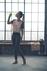 Fototapeta na wymiar Woman in profile standing in loft gym drinking from water bottle