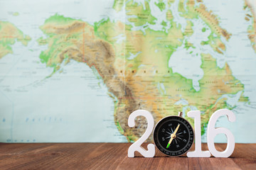 Travel in 2016 year. Numbers 2016 with magnetic compass. Blurred world map as background.
