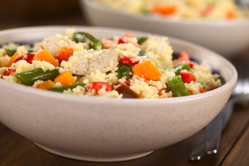 Two bowls of couscous dish with chicken, green bean, carrot and red bell pepper (Selective Focus, Focus on the chicken meat in the middle of the dish)