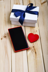 Red Smart Phone With Blank Screen, White Gift Box With Blue Ribbon And Little Red Heart On Wooden Boards. Love Concept.