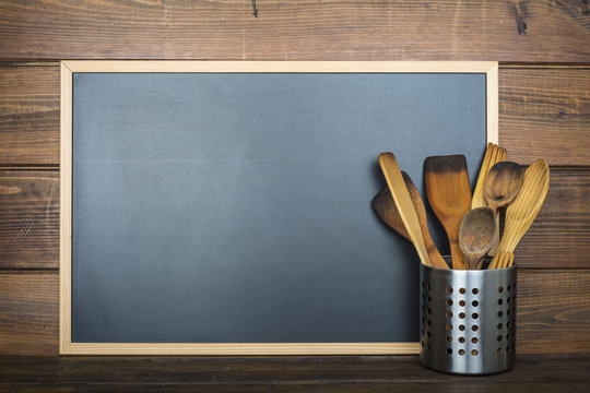 Pizarra vac&iacute;a con espacio para texto sobre fondo de madera y utensilios de cocina