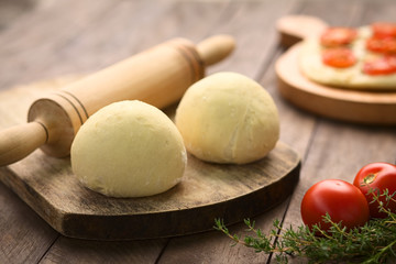 Yeast dough for pizza or flatbread with rolling pin on wooden board (Selective Focus, Focus on the front of the first dough ball)