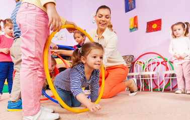 Kids crawl though hoop with teacher and friends 